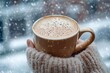 © Юлія Ткачук - Atmospheric winter background: a hand holding a cup of hot coffee on the background of a window with snow. Comfort and warmth.