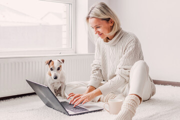 happy middle aged woman with dog using her laptop at cozy white home