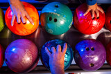 Photo with bowling balls in different colors and a person's hand reaching for them for a fun night out.