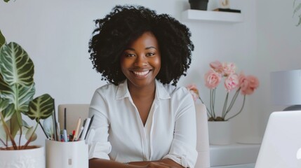 Wall Mural - A woman with curly hair is sitting at a desk with a laptop and a potted plant