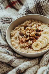 Bowl of healthy balanced diet oatmeal meal with chopped hazelnuts, peanut butter, cut banana slices and chocolate.