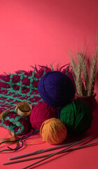 A Piece of knitting with color threads ball of yarn and a knitting needle on red background.