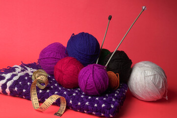 A Piece of knitting with color threads ball of yarn and a knitting needle on red background.