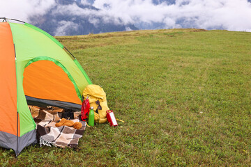 Wall Mural - Tent, backpack and camping equipment on green grass in mountains, space for text