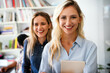 © NDABCREATIVITY - Two happy successful business female collegues standing next to each other in an office