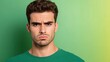 © fotogurmespb - Frustrated young man with a furrowed brow and raised eyebrow, glaring directly ahead, isolated on a green-to-yellow gradient background