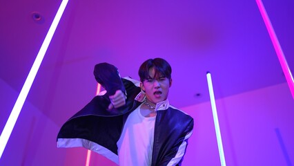 Low angle camera of professional street dancer looking at camera with casual cloth. Skilled performer moving to city pop music while standing at studio with purple led light. Close up. Regalement.