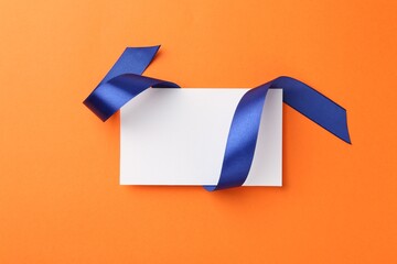 Canvas Print - Blank card and blue ribbon on orange background, top view