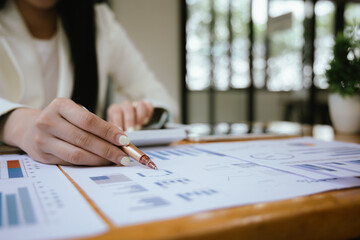 A businesswoman sits at her desk, calculating financial data on her laptop. Surrounded by paperwork and charts, she analyzes expenses and income, reflecting her role in corporate finance and accountin