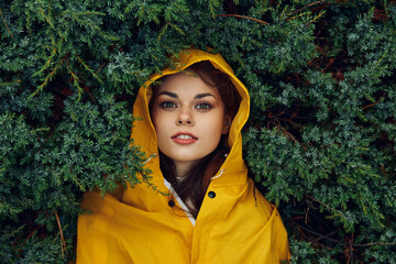 A young woman in a stylish yellow raincoat hiding behind lush evergreen trees in a tranquil forest setting