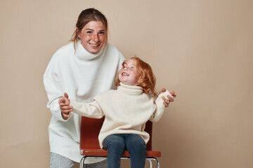 Wall Mural - Family time mother and daughter relaxing together on chair in front of beige background