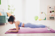 © deagreez - Young woman in activewear practicing plank exercise at home in bright, modern living room setting