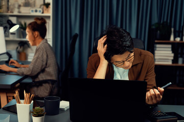 Businessman with stressful face looking on document file deadline while coworker trading stock exchange investment at late night time at modern office working on startup company project job. Infobahn.