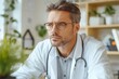 © SerPak - A dedicated male doctor dressed in a white coat sits thoughtfully in his modern clinic, surrounded by greenery.