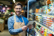 © Liubomir - Grocery store worker in apron smiling while using digital tablet for inventory management. Enhancing customer service with technology in retail setting. Efficient and friendly service