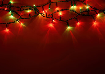 Wall Mural - christmas lights are shining on a red background with copy space