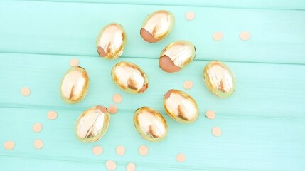 Poster - Chocolate Eggs Enveloped in Golden Foil on a Light Blue Wooden Surface Overhead View