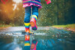 © Babb - A young girl is splashing in puddles while wearing colorful rain boots