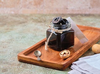 Wall Mural - Green walnut jam in a glass jar on a wooden tray on a green concrete background. Exotic sweets, recipes from around the world.