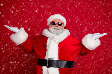 Poster - Photo of cheerful man two hands demonstrate empty space variants wear santa hat costume isolated red color background