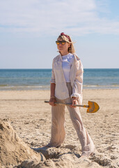 Young pretty woman having fun on beach. Builds tower of sand, digs sand with child shovel. Fun, vacation