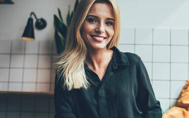 Portrait of successful female student with cute smile on face taking rest in cozy coffee shop and looking at camera, positive Caucasian hipster girl holding textbook for education and posing