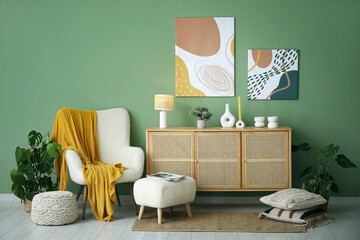 Poster - Comfortable armchair, pictures, pouf and wooden chest of drawers in interior of living room