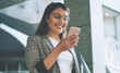 © BullRun - Cheerful Turkish woman dressed in elegant jacket smiling from received email with funny content, happy millennial female with modern mobile phone in hands feeling good from messaging on website