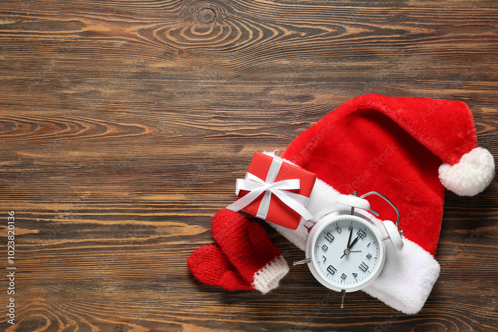 Alarm clock, mittens, Santa hat and gift box on wooden background. Top view