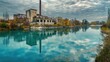 © Rodica - An old, abandoned factory building with a tall chimney reflects on the calm surface of a river, surrounded by autumn trees and a cloudy sky, symbolizing decay and industrial past