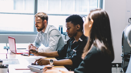 Group of young management experts spending time for conference meeting in office for discussing innovations in finance world, male and female partners collaborating and planning accounting trade