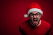 © iamfrk7 - Angry man in Santa hat screaming in frustration on red background. Humorous Christmas portrait perfect for funny holiday cards or advertising with seasonal humor.