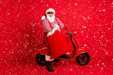 Poster - Full length photo of grandfather grey beard stand near retro moped hold sack gifts wear santa claus x-mas costume suspenders sunglass striped shirt boots cap isolated red color background