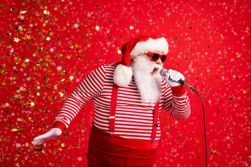 Photo of grandpa grey beard hold mic open mouth scream sing song karaoke wear santa claus x-mas costume suspenders sunglass striped shirt cap isolated red color background