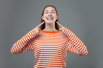 Smiling girl pointing at her braces on grey background