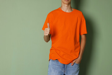 Canvas Print - Teenage boy wearing orange t-shirt and showing thumbs up on green background, closeup. Space for text