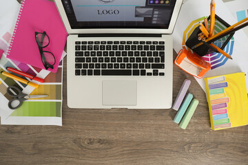 Poster - Fashion designer`s workplace with laptop, color palette and different stationery on wooden table, flat lay