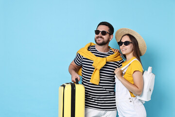 Wall Mural - Happy man with suitcase and woman on light blue background, space for text