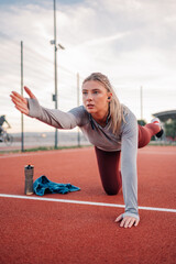 Wall Mural - Young sporty woman stretching her body on running track