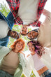 © Jose Calsina - Vertical. Low angle view of a group of multiracial happy young teenagers hugging each others in a circle, looking down at camera with smiling faces representing friendship, diversity, and togetherness