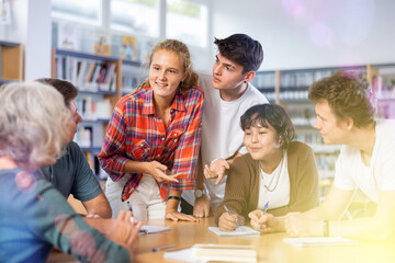 Wall Mural - Group of fifteen-year-old schoolchildren with a female teacher are discussing something in the school library during an extracurricular lesson