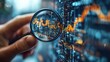 © Alienmarsh - A hand holding a magnifying glass over a computer screen displaying a stock market graph, highlighting the details and trends.
