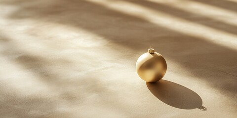 Poster - A gold ornament sits on a tan surface, casting a shadow. Concept of warmth and coziness, as the ornament is a symbol of the holiday season