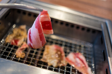 Hand using chopsticks to pick up raw pork put to grill