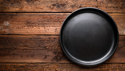 Empty rustic black cast iron plate over old wooden background. Top view. Copy space