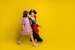 © deagreez - Full size profile photo of two little kids hold arms walk empty space halloween pirate princess costume isolated on yellow color background