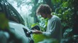 © Sansern - A man charges an electric car in a lush, green forest. The man is dressed in casual clothing and is looking at the charging cable.