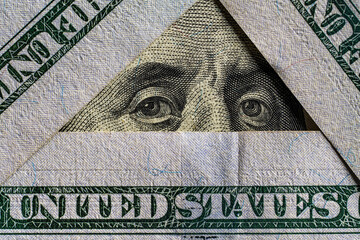 President of Benjamin Franklin's eyes in a triangle of hundred dollar bills, closeup, top view