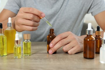 Poster - Young man dripping CBD tincture into bottle from dropper at wooden table, closeup