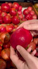 Wall Mural - the process of examining and buying a red juicy pomegranate in a supermarket